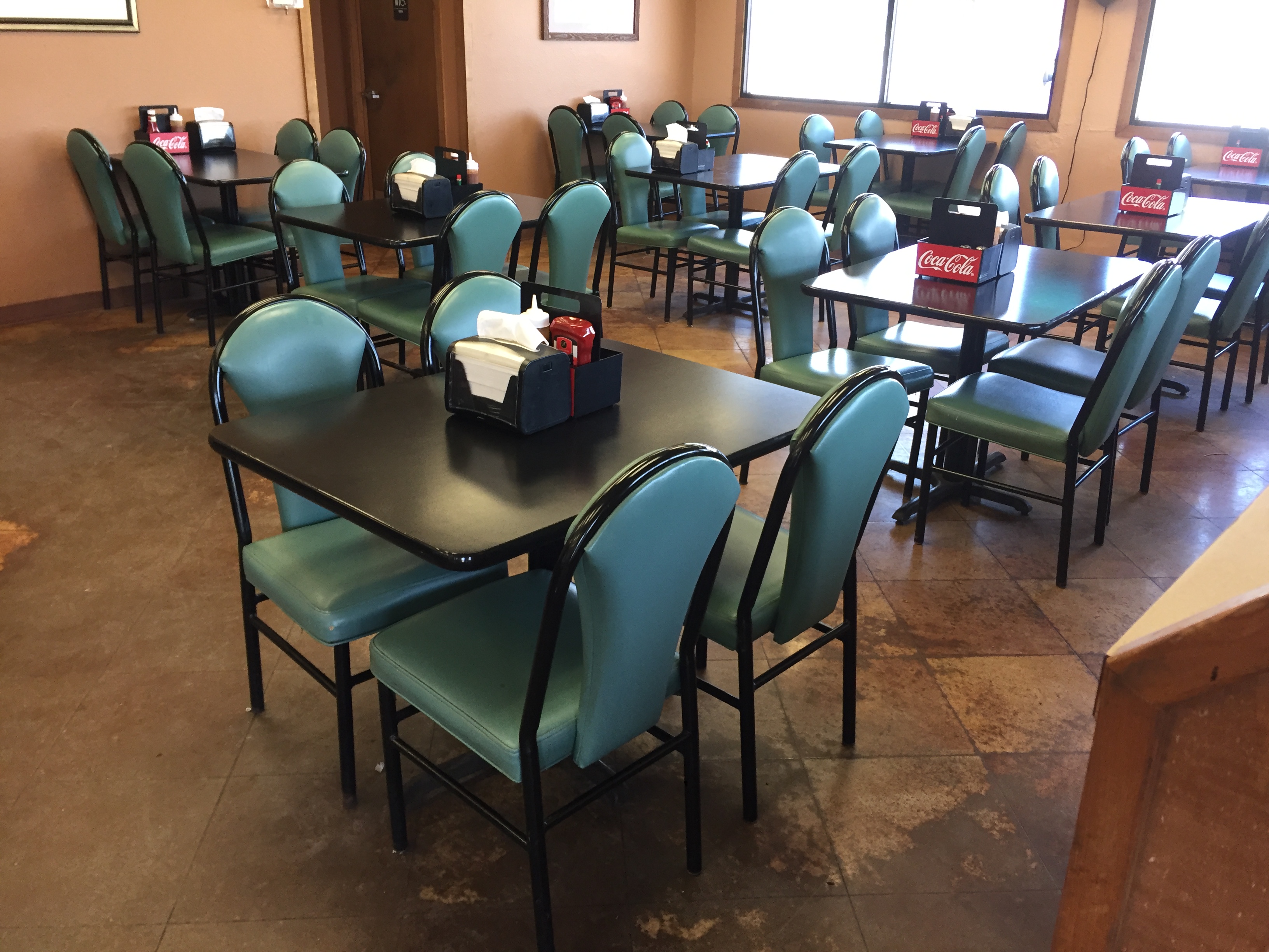 Inside The Sticks BBQ dining room — teal padded chairs, black tables with Coca-Cola caddies, warm orange walls, Brownwood TX