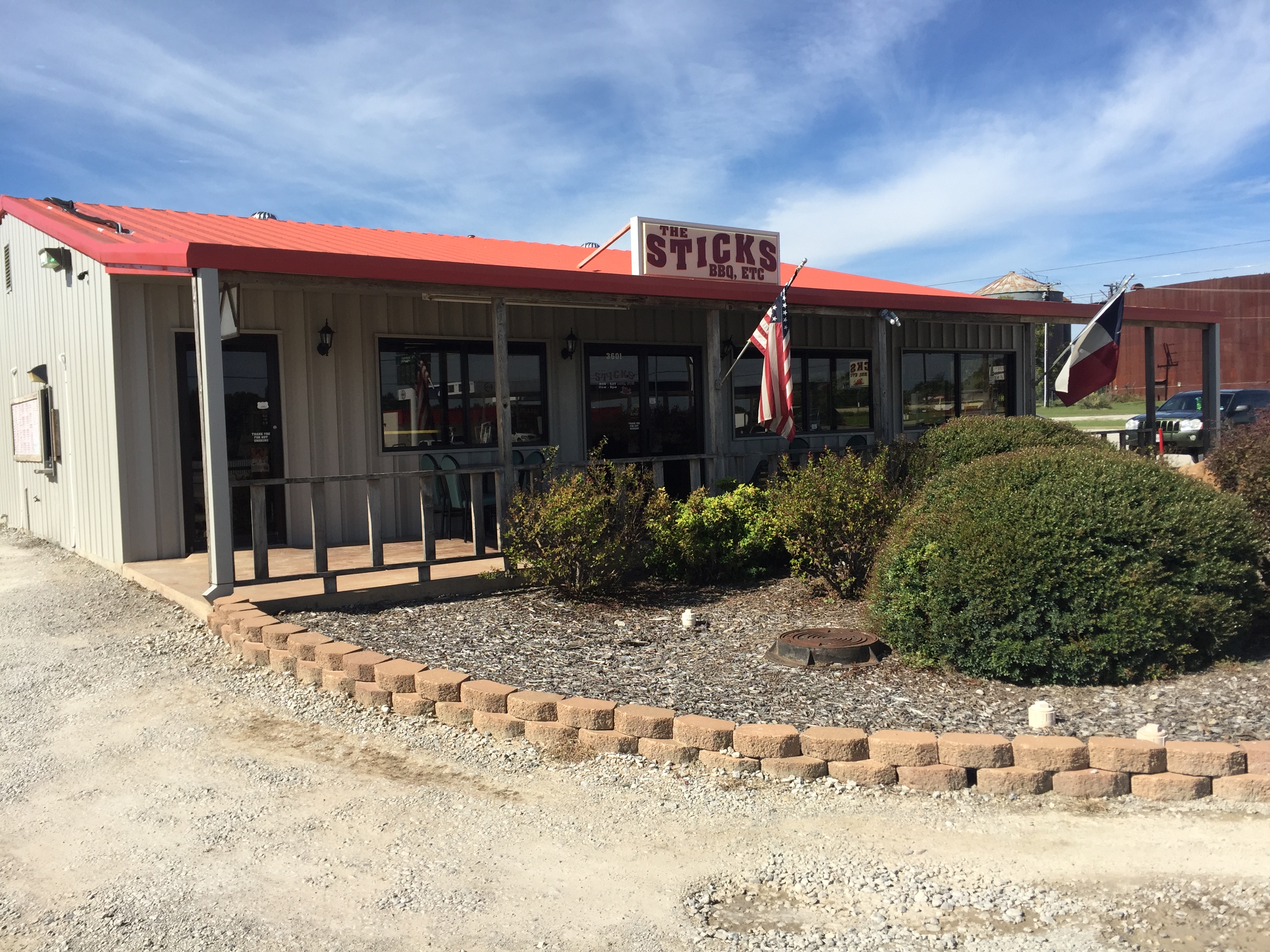 The Sticks BBQ restaurant exterior at 3501 US-377, Brownwood, TX — red metal roof, American and Texas flags